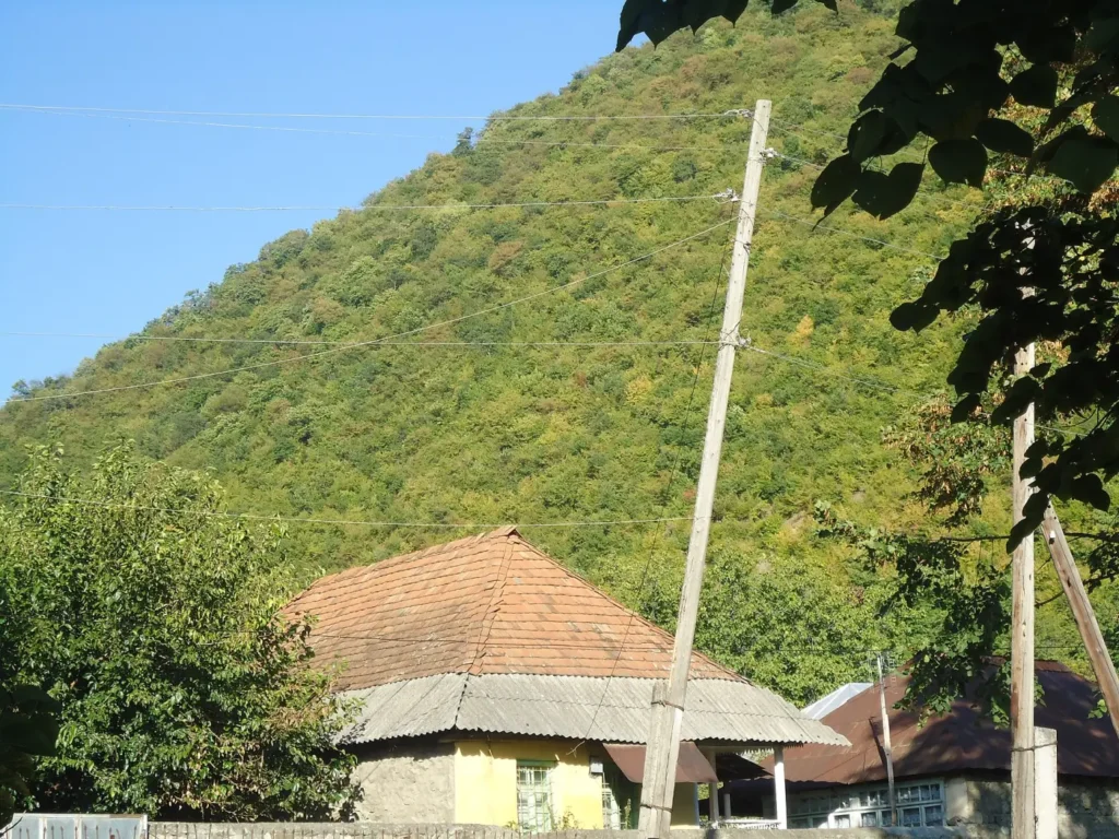 Village house with a red roof below wooded mountains in northern Azerbaijan